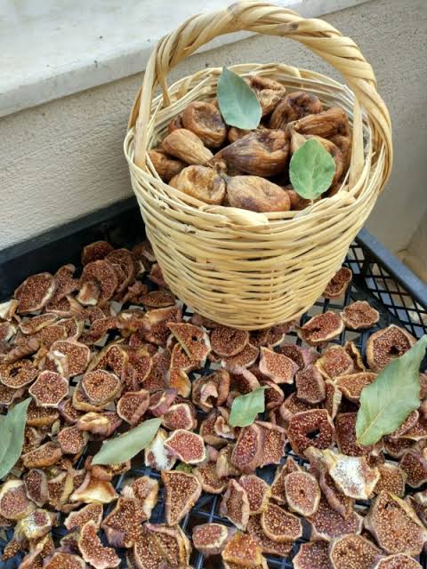 A wicker basket of whole dried figs standing on a drying tray covered with halved figs